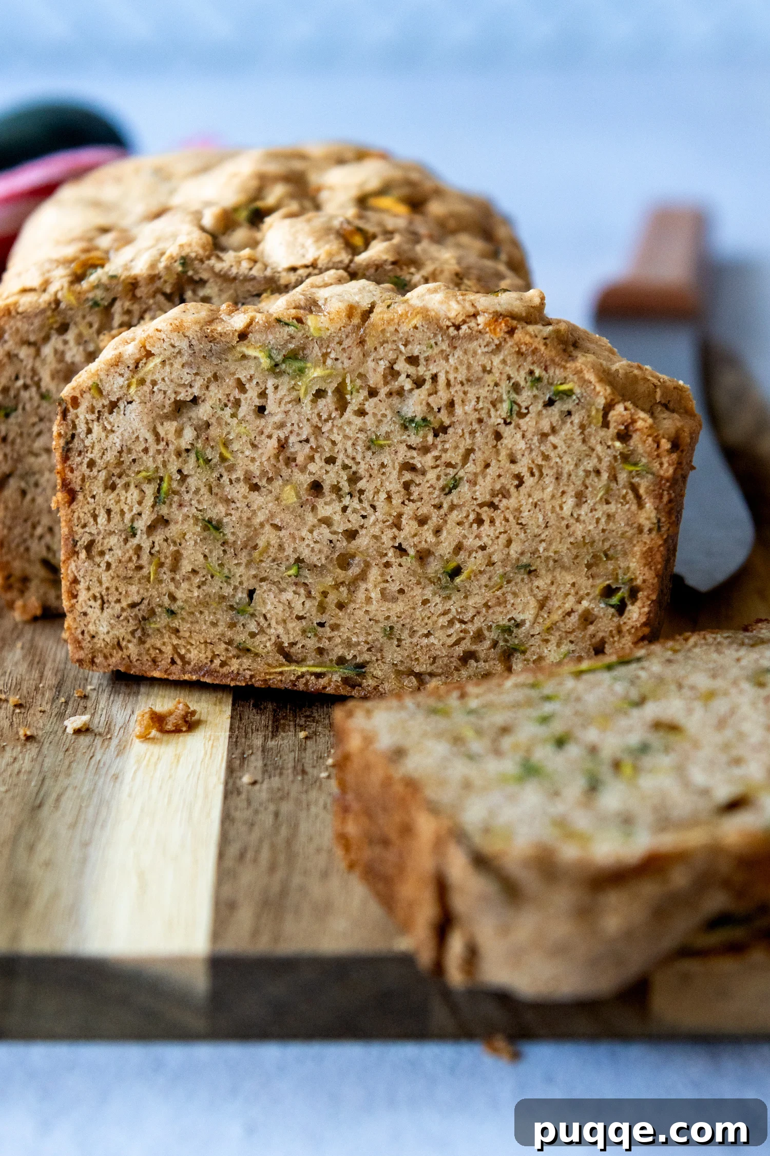 A perfectly baked slice of moist zucchini bread positioned upright on a wooden cutting board.