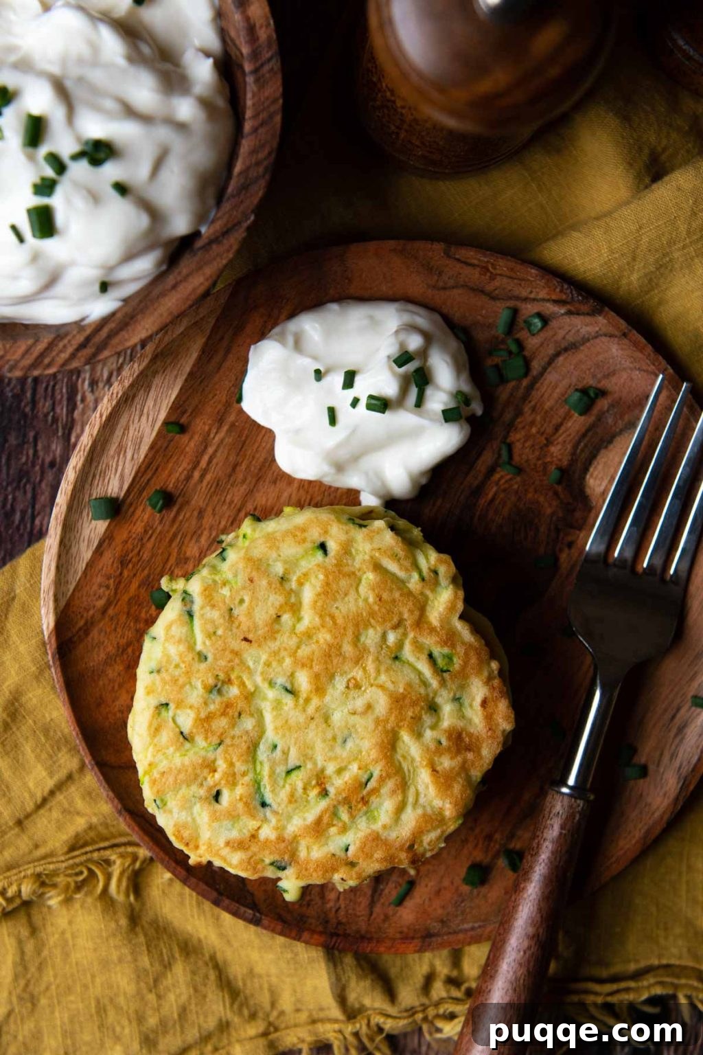 Golden-brown gluten-free zucchini fritters artfully arranged on a rustic wooden plate, with a creamy dollop of sour cream on the side, ready to be enjoyed.