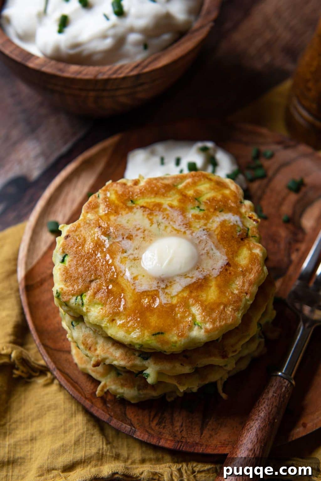 A close-up side angle shot of freshly cooked gluten-free zucchini fritters, still warm and topped with melting butter, highlighting their golden-brown exterior and delicious appeal.