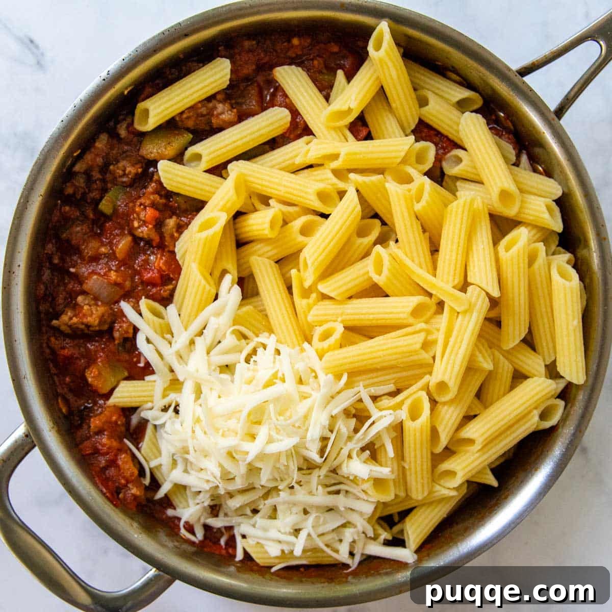 Speedy Supreme Skillet Pizza Pasta 4 Cooked al dente pasta being gently mixed into a rich, simmering tomato sauce with sausage, pepperoni, and vegetables in a large skillet.