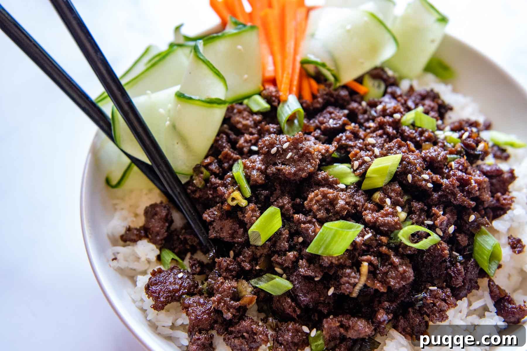 Flavorful Gluten-Free Korean Ground Beef Bulgogi 6 close up of a bulgogi bowl with various garnishes on top, and chopsticks resting on the side, set against a simple background.