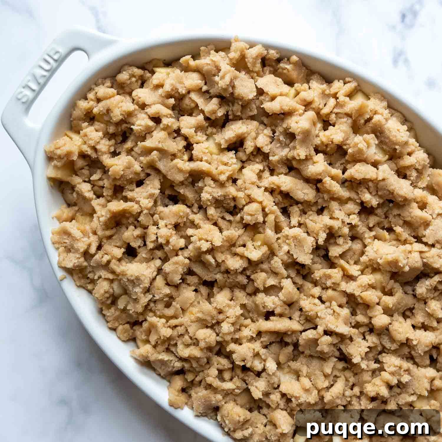 Unbaked apple crisp with a generous layer of streusel topping in a white oval baking dish, ready for the final bake.