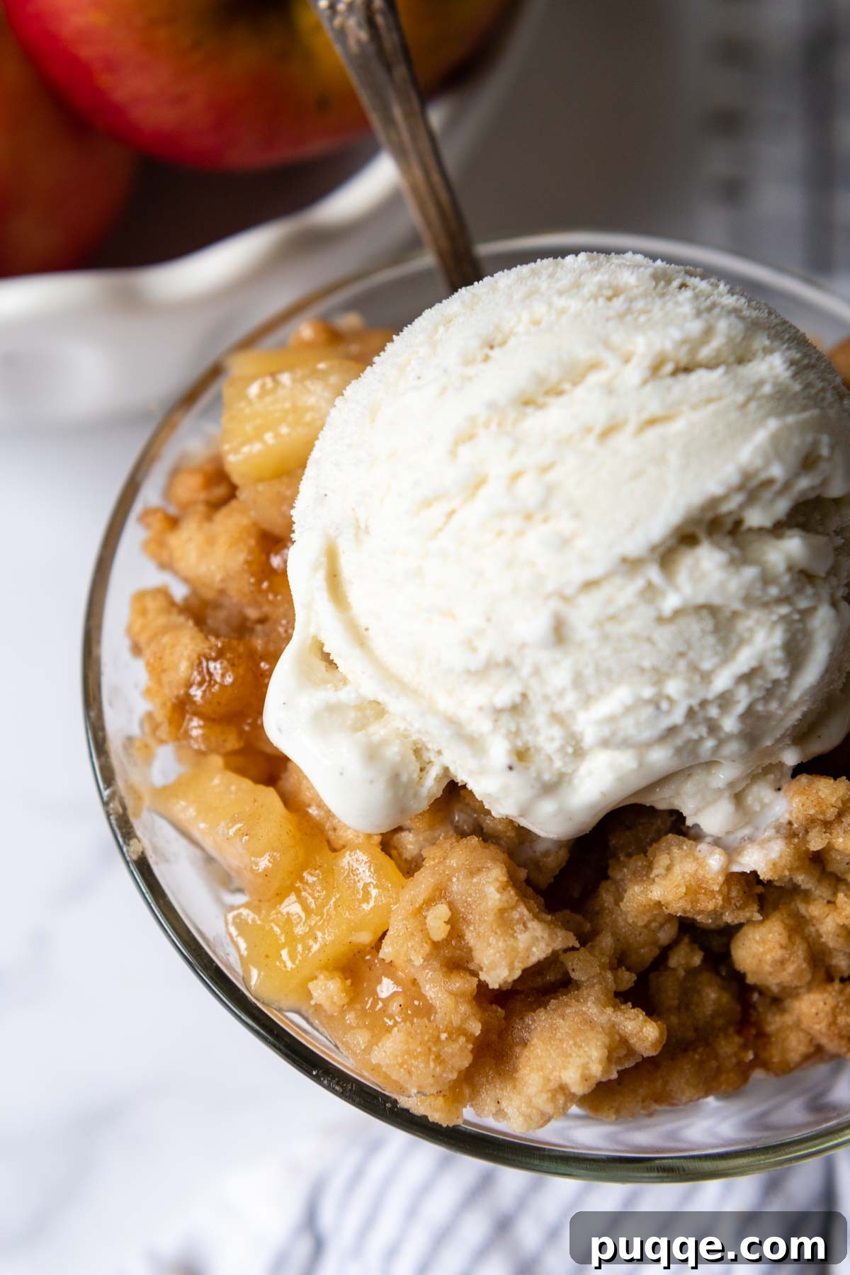 An overhead shot of a glass bowl filled with warm gluten-free apple crisp, topped with a melting scoop of vanilla ice cream.