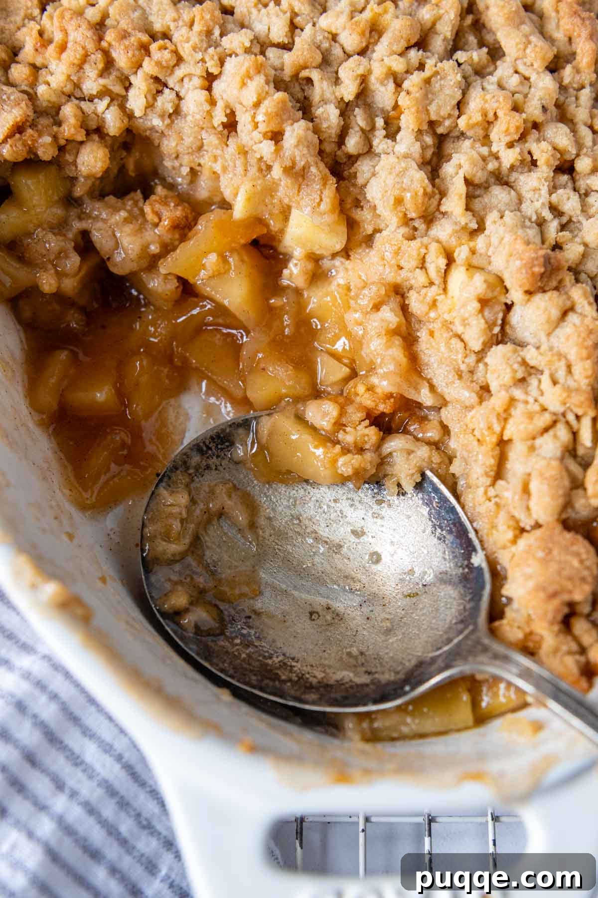 A spoon scooping into a close-up of the textured, golden-brown gluten-free apple crisp, revealing the warm, spiced apple filling beneath.