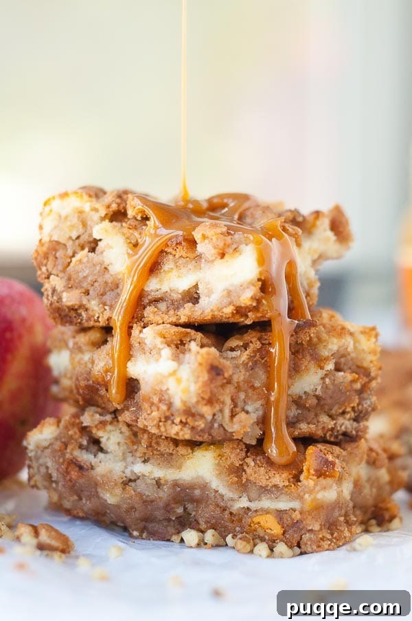 A stack of golden caramel apple blondie cheesecake bars with caramel dripping down, showing the distinct layers.