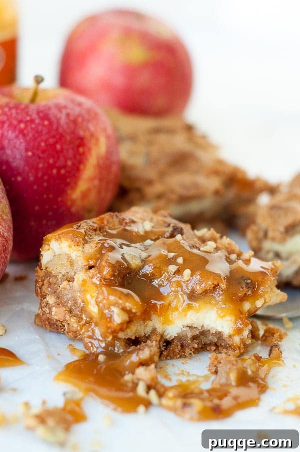 A bite taken out of a caramel apple blondie cheesecake bar, clearly revealing the distinct layers of blondie, creamy filling, and fresh apple chunks.