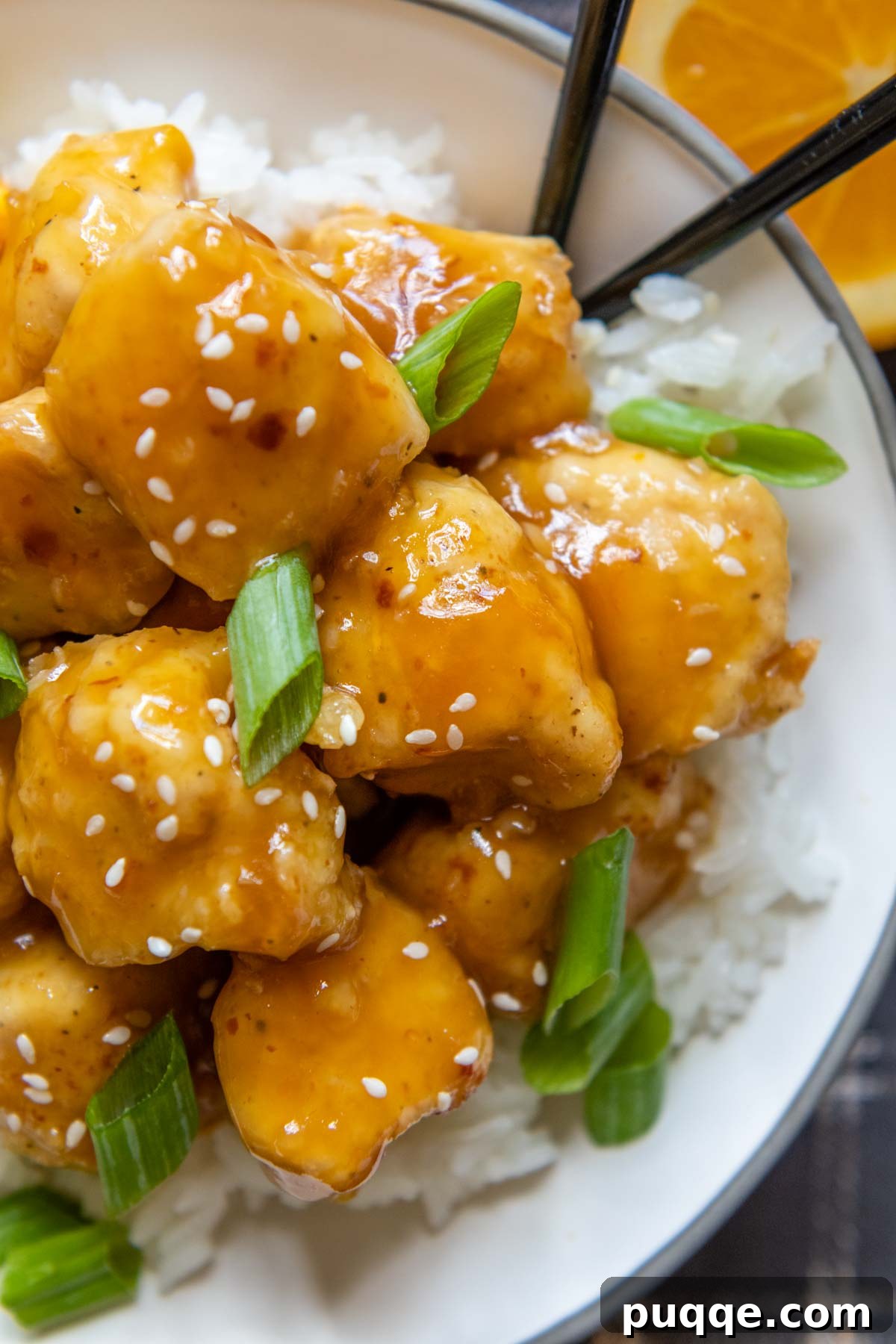 Close-up of crispy gluten-free orange chicken pieces coated in a vibrant orange sauce, ready to be served.