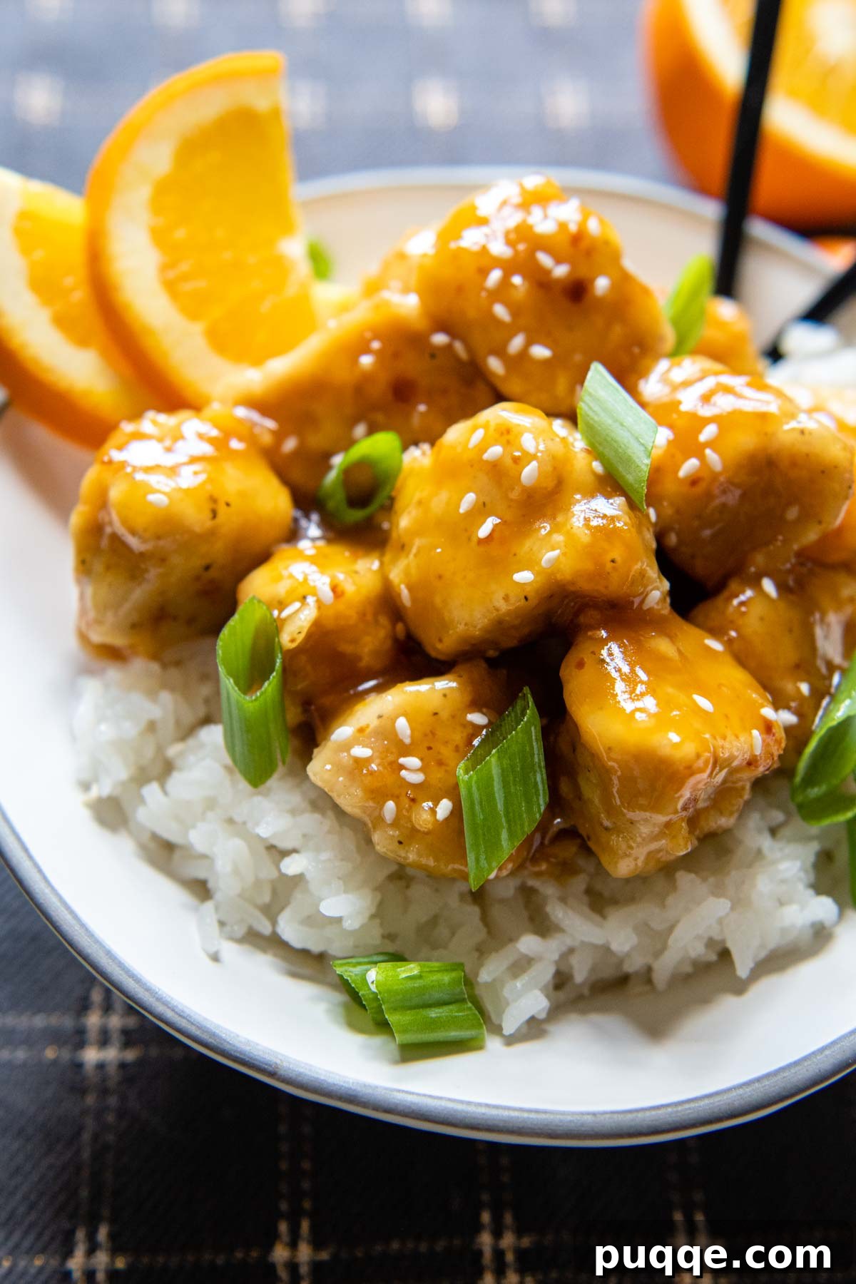 A serving of gluten-free orange chicken in a white bowl, garnished with fresh orange slices and green onions.