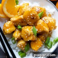 overhead shot of a serving of crispy gluten-free orange chicken in a white bowl with chopsticks.