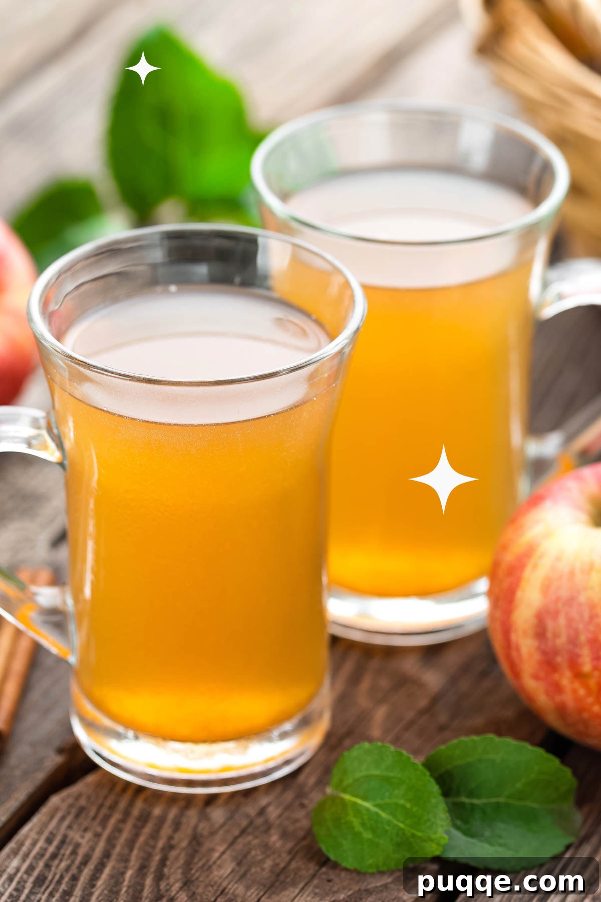 Two clear glasses filled with golden apple cider and a whole red apple next to them, signifying a wholesome, refreshing drink.