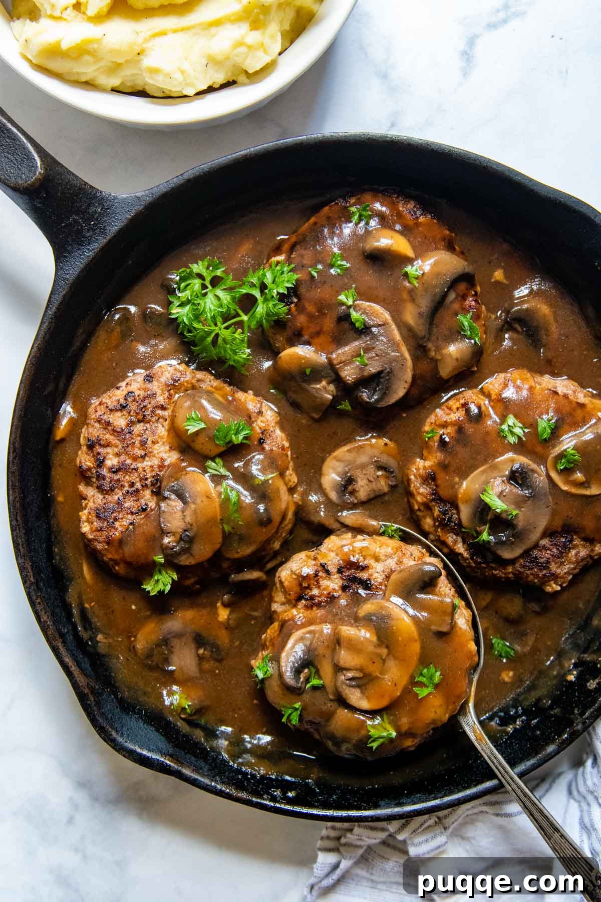 Cooked Salisbury steaks with a generous amount of mushroom gravy, ready to be served from a cast iron skillet.