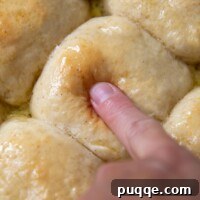 A finger pressing into the top of a freshly baked, soft gluten-free roll, showing its squishy texture.