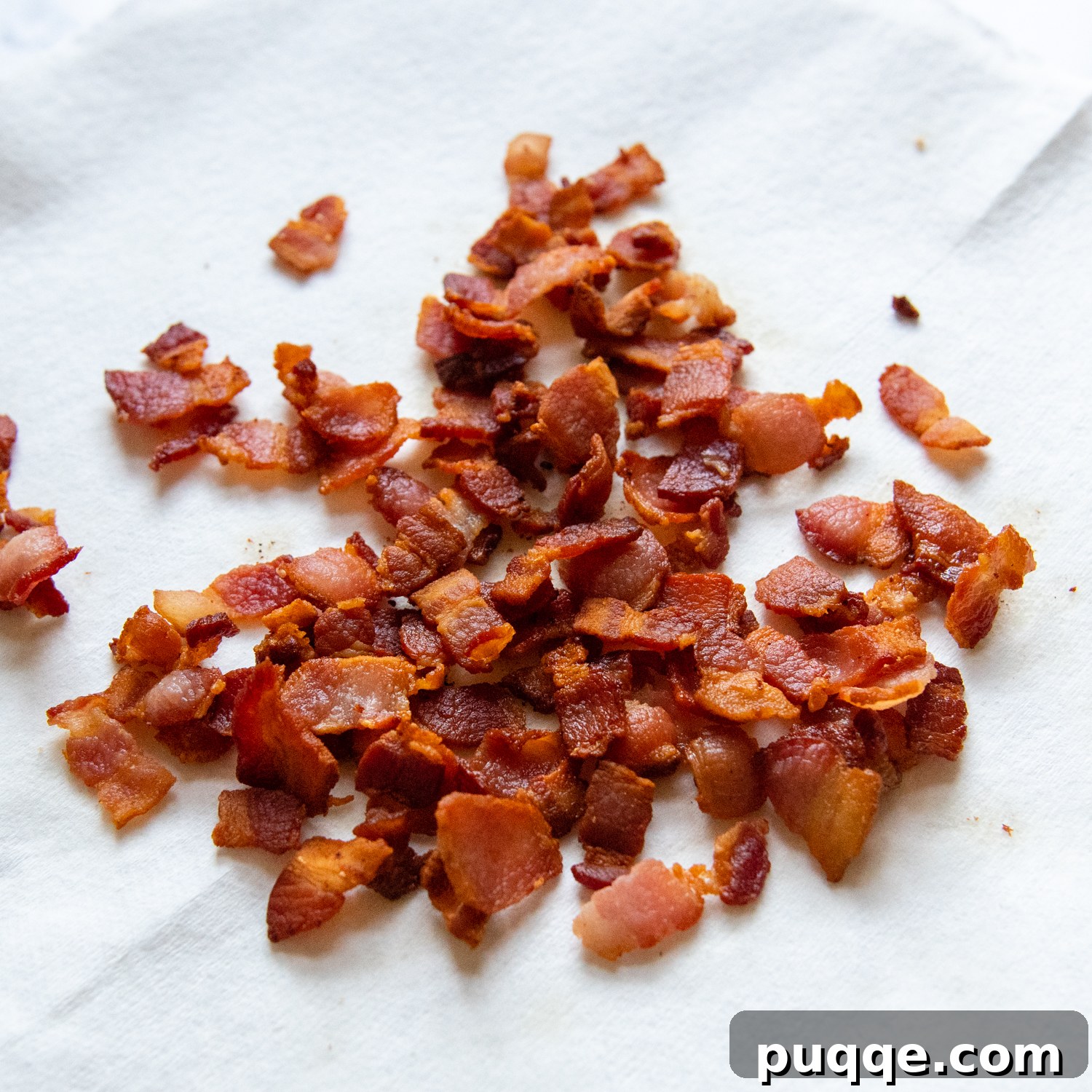 Crispy bacon strips draining on a paper towel to absorb excess grease.