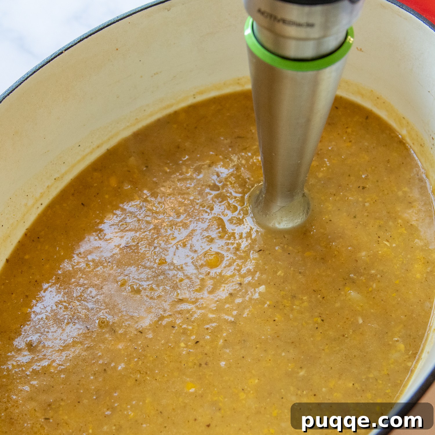 An immersion blender actively blending a portion of the corn chowder in the pot.