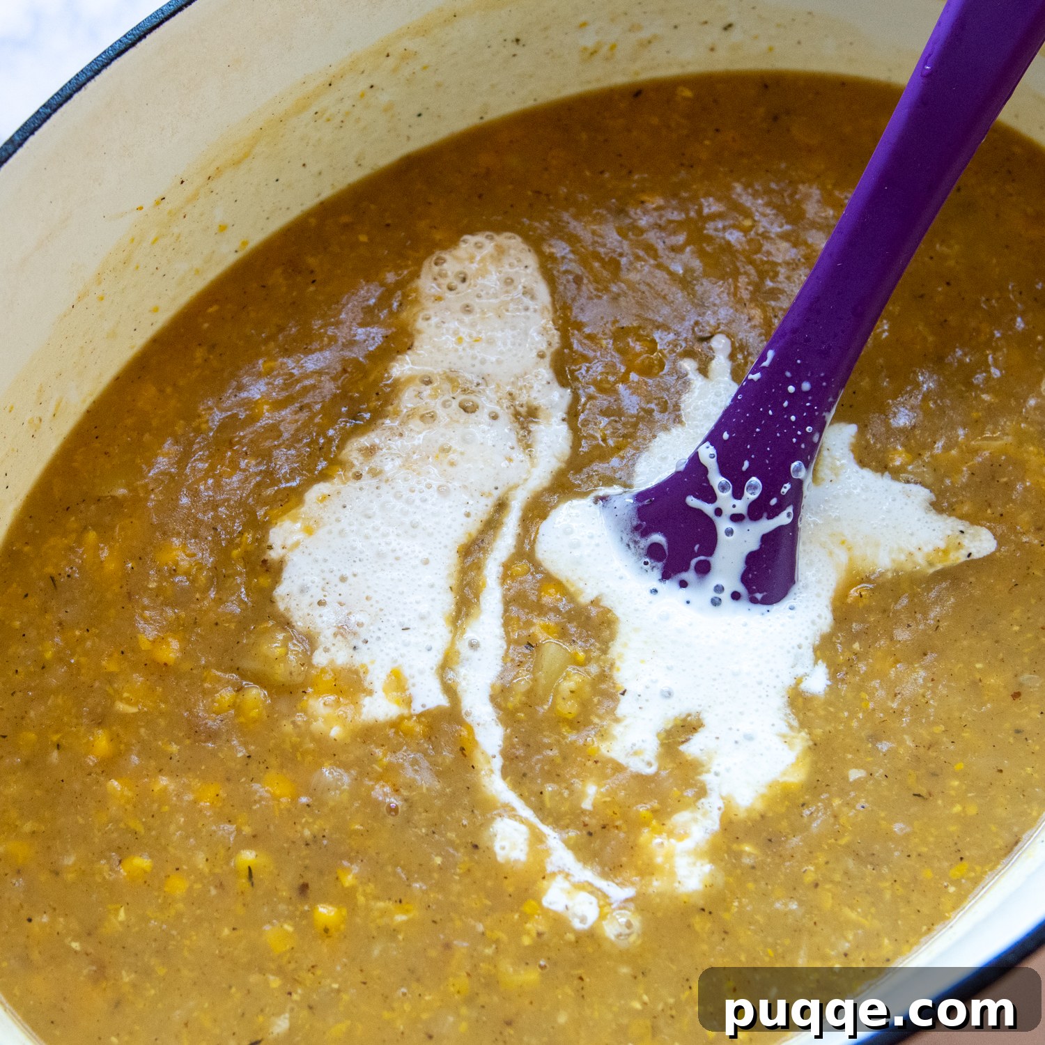 Pouring and stirring heavy cream into the corn chowder to achieve a rich, creamy texture.