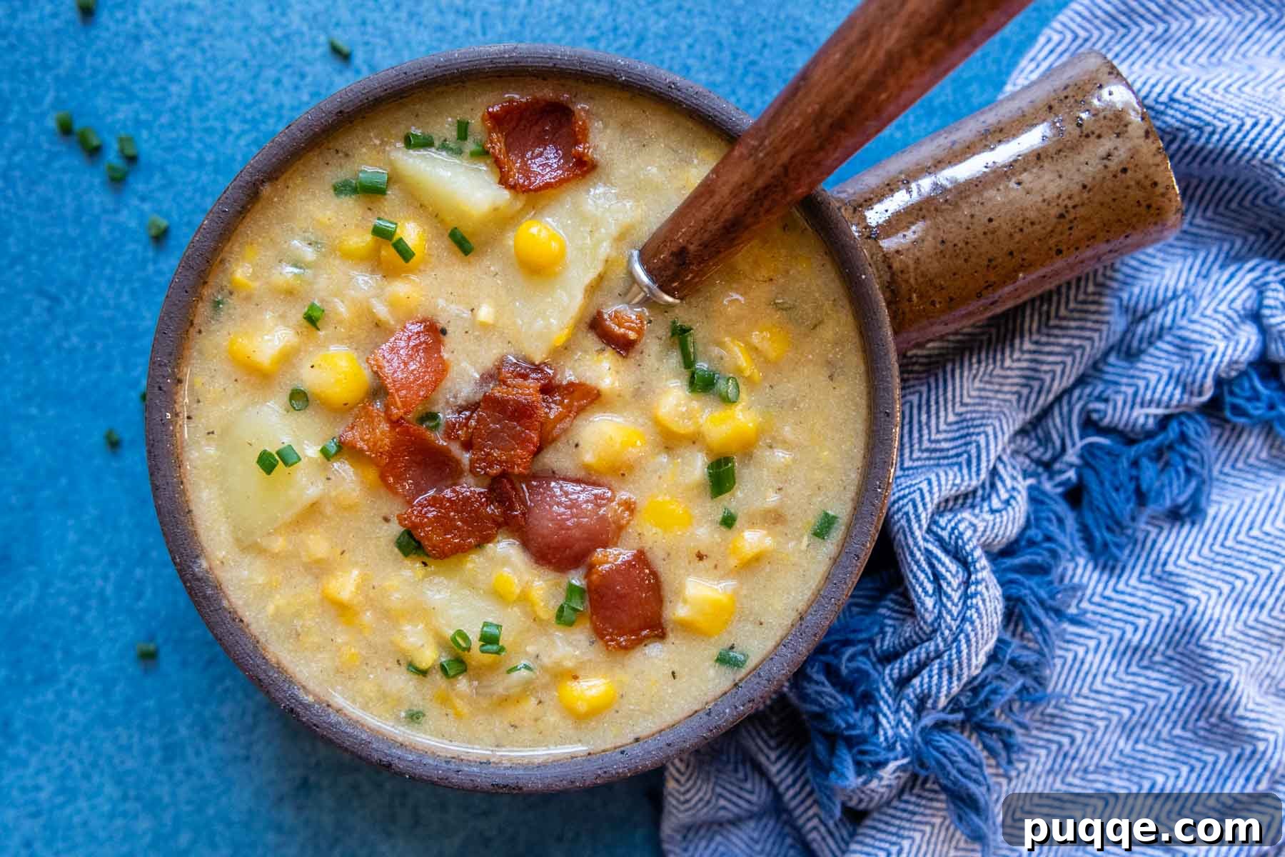 A spoon dipping into a bowl of creamy corn chowder, set against a blue background, inviting a taste.