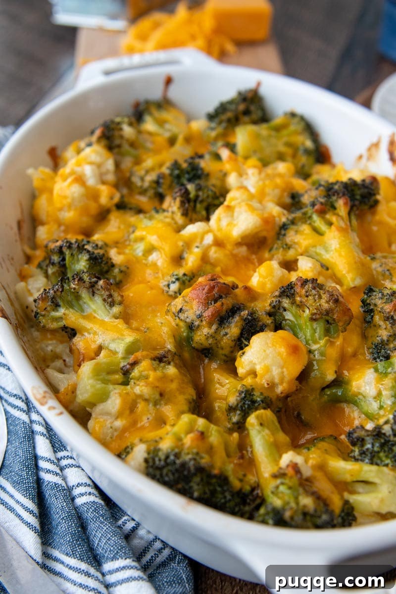 Close-up of bubbling melted cheddar cheese over tender broccoli and cauliflower in a casserole dish.