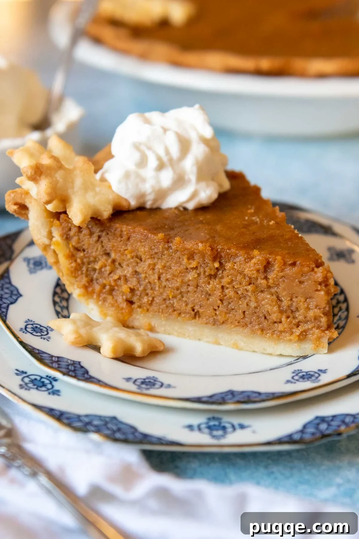 A beautifully plated slice of southern gluten-free sweet potato pie with whipped cream, with the whole pie blurred in the background.
