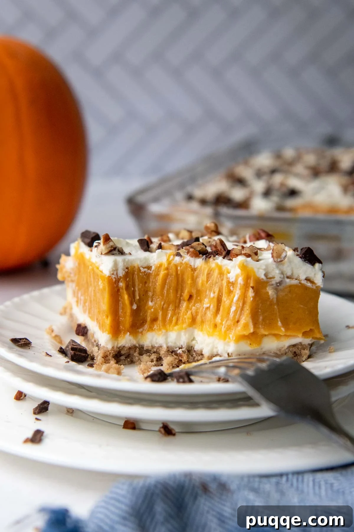 A bite taken out of an ultra-creamy pumpkin lush dessert, with a small decorative pumpkin in the background, signaling autumn flavors.