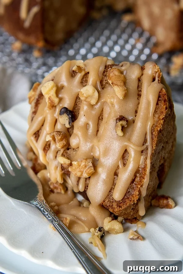 A delectable slice of fresh apple cake on a white plate, generously drizzled with brown sugar praline glaze and scattered with walnuts.