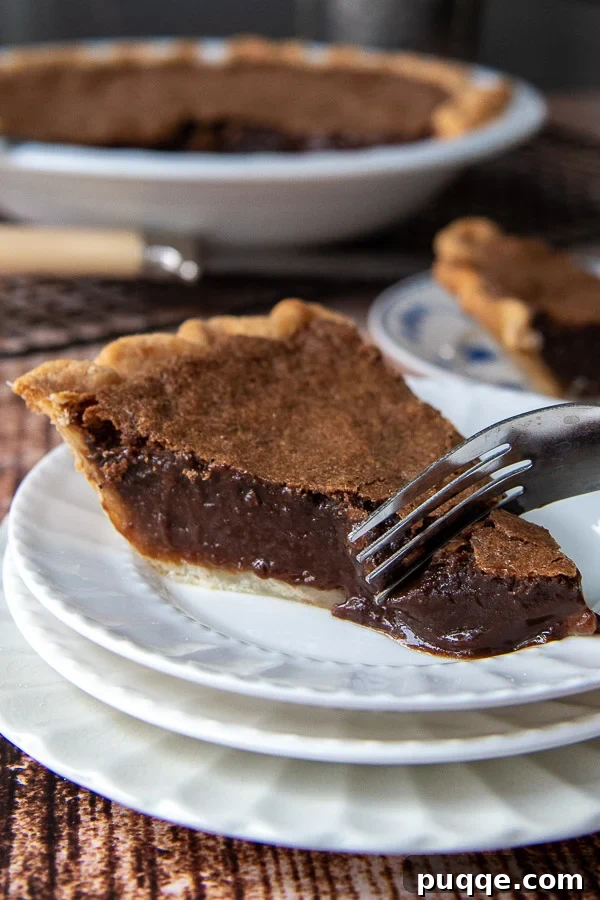 A fork cutting into a rich piece of vintage fudgy chocolate chess pie, highlighting its dense, satisfying texture.