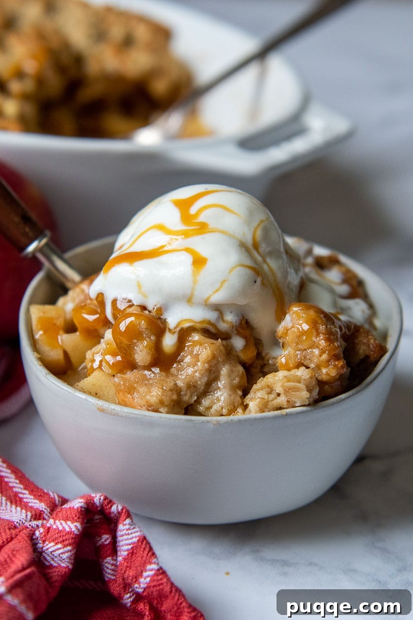 A warm bowl of gluten-free apple crisp, topped with a scoop of ice cream and drizzled with caramel sauce.