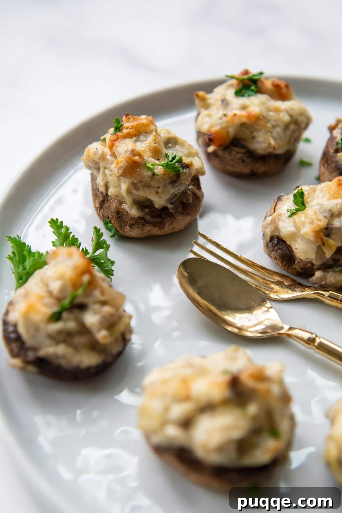 A close-up of a perfectly baked gluten-free stuffed mushroom, laden with creamy artichoke parmesan mixture, on a white serving platter.