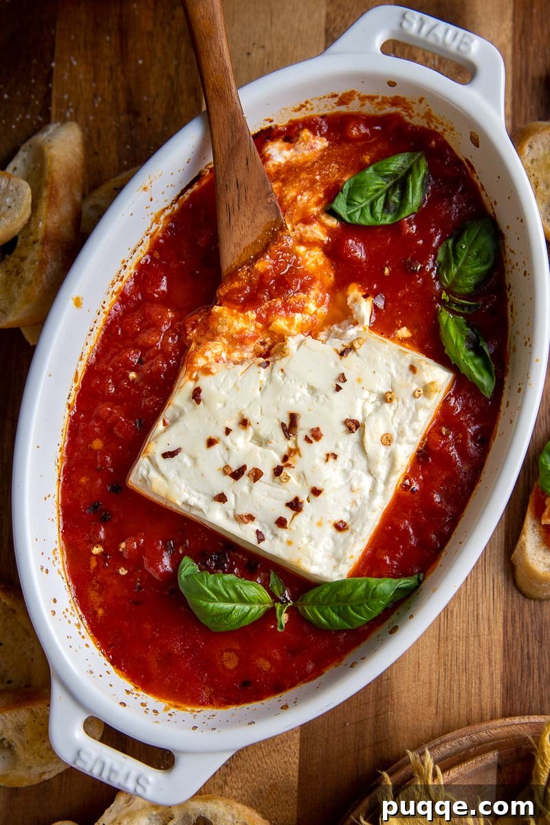 Overhead shot of creamy baked feta cheese surrounded by vibrant marinara sauce in a small baking dish.
