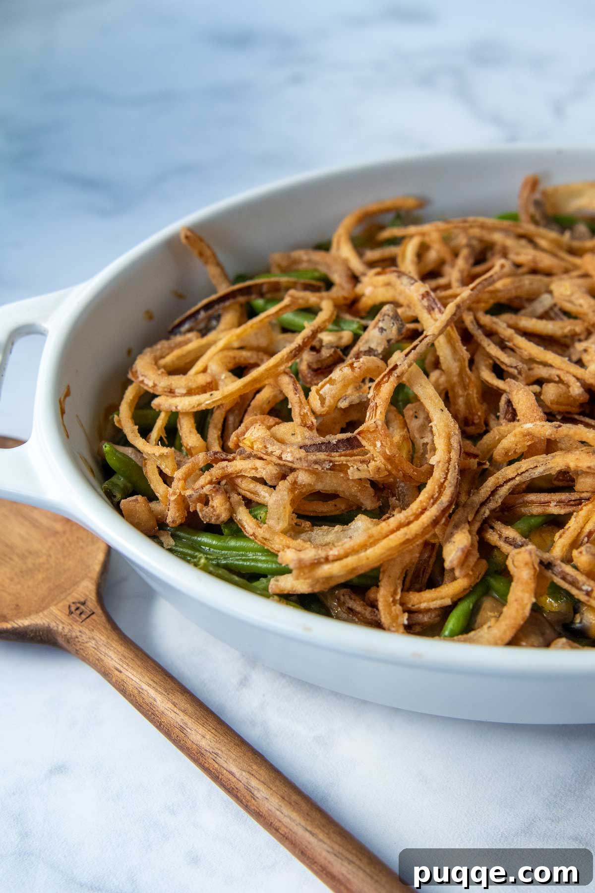 A close-up shot of a bubbling gluten-free green bean casserole with crispy fried onions on top, set on a marble surface.