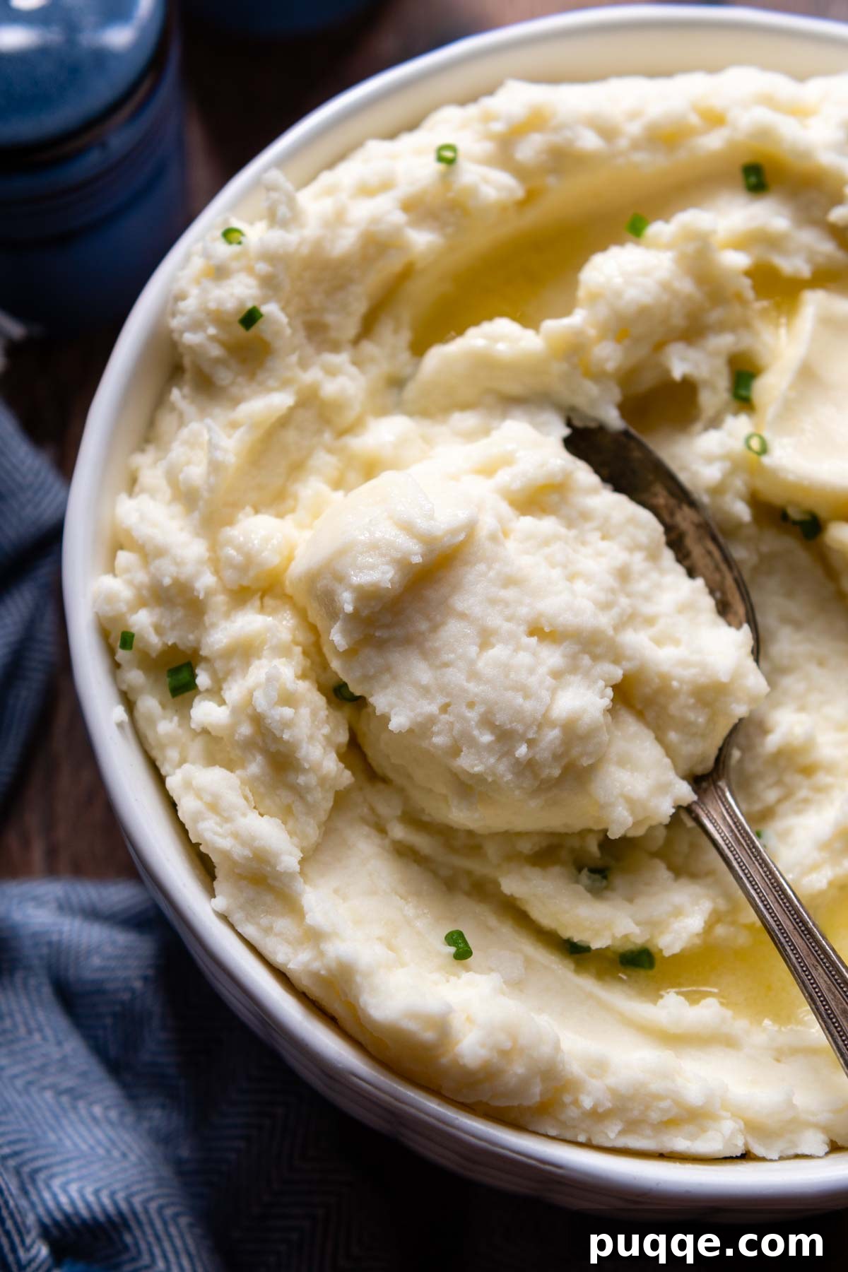 A spoon diving into a bowl of exceptionally creamy and fluffy gluten-free mashed potatoes, hinting at their rich flavor.