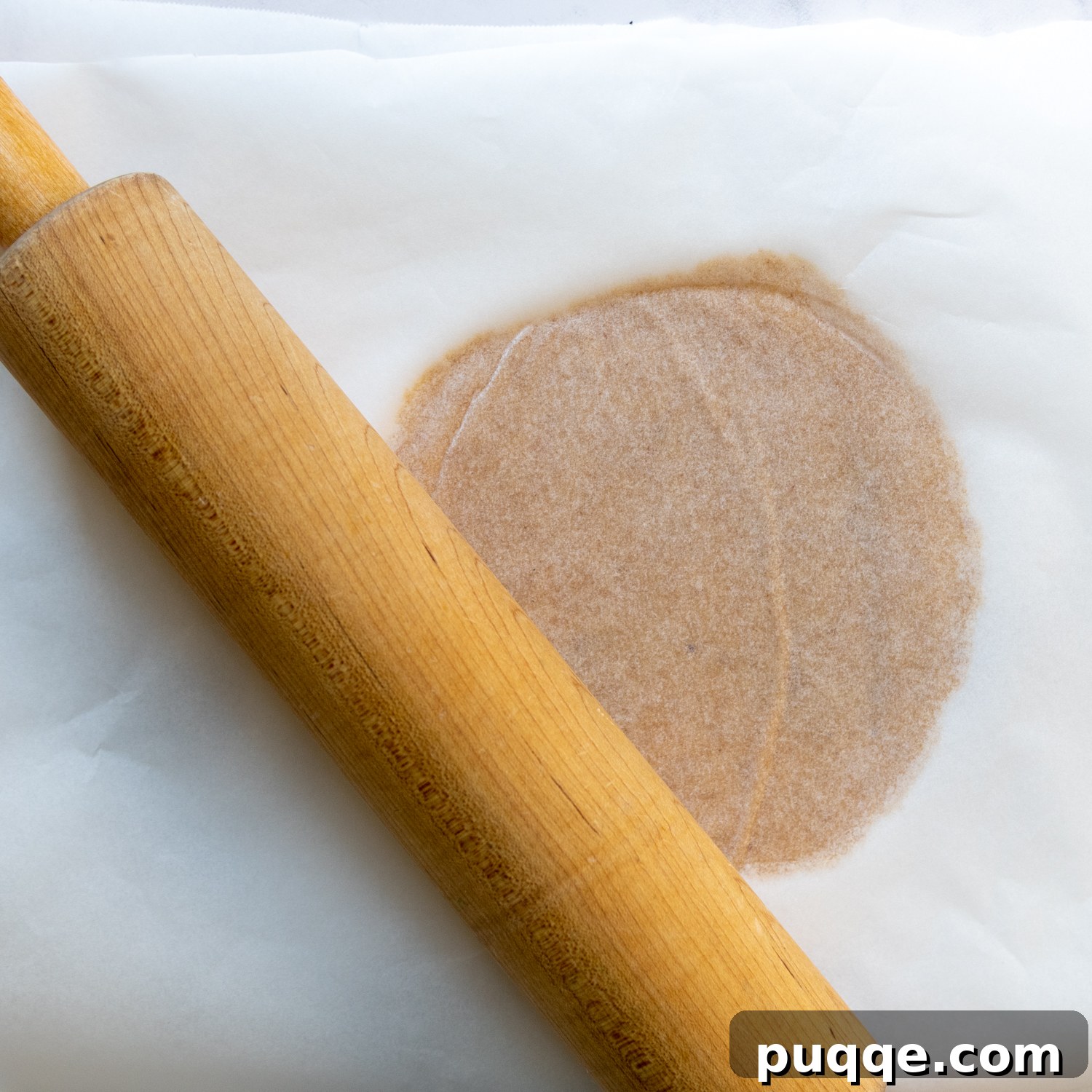 A rolling pin gently flattening the dough between two sheets of parchment paper.