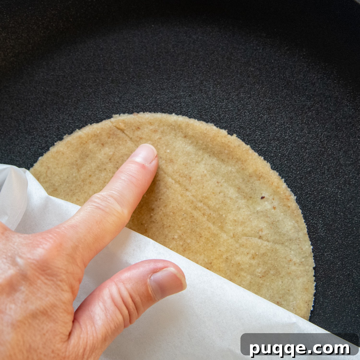 A finger smoothing out minor creases on the dough while it cooks in the pan.