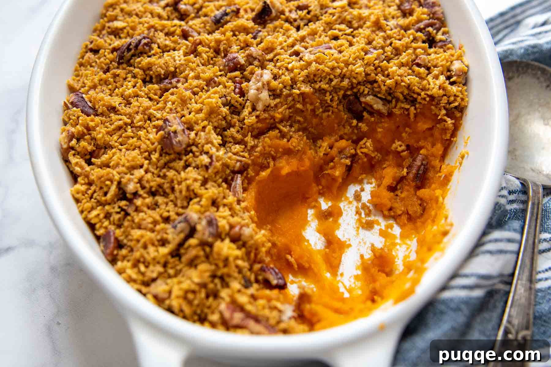An overhead shot of a white casserole dish with a generous portion of gluten-free sweet potato casserole scooped out, showcasing the crispy topping.