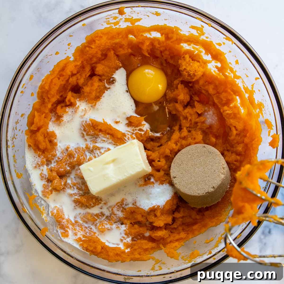 Egg, heavy cream, brown sugar, and softened butter being added to the mashed sweet potatoes in a bowl.
