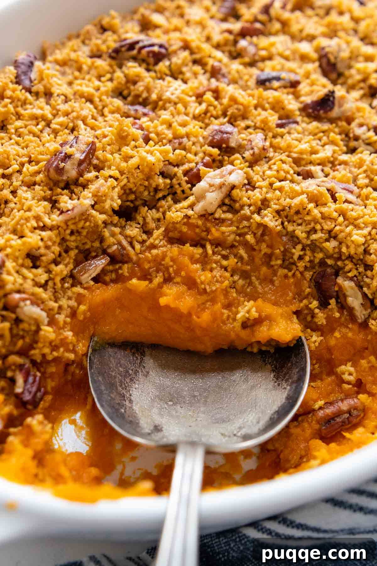 A spoon digging into a serving of gluten-free sweet potato casserole, showing the moist interior and crunchy topping.