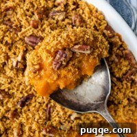 A spoon lifting out a serving of sweet potato casserole, highlighting the texture and topping.