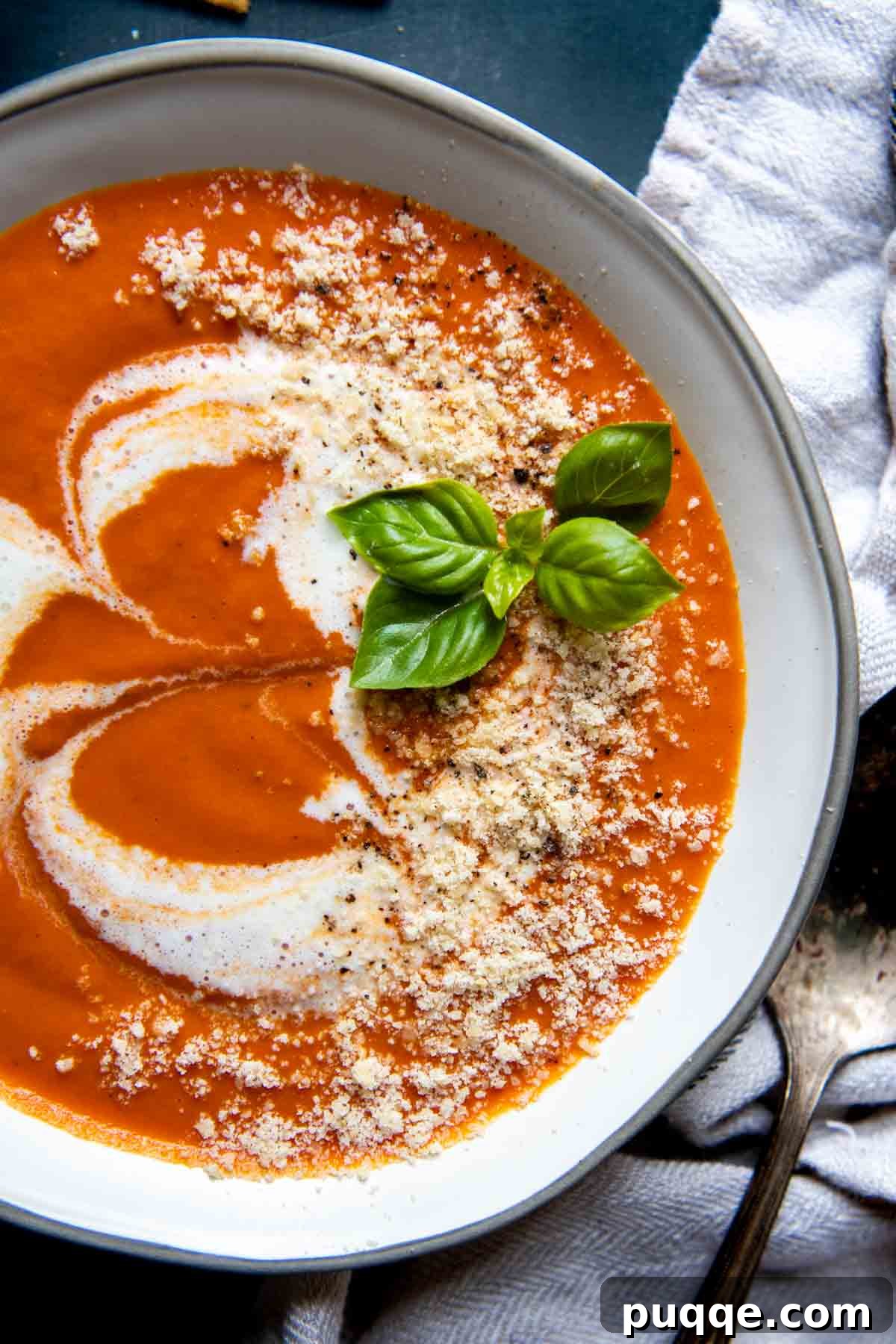 Amazing Gluten-Free Tomato Soup From Your Pantry 6 Overhead shot of a bowl of creamy gluten-free tomato soup, garnished with grated parmesan cheese and fresh basil leaves.