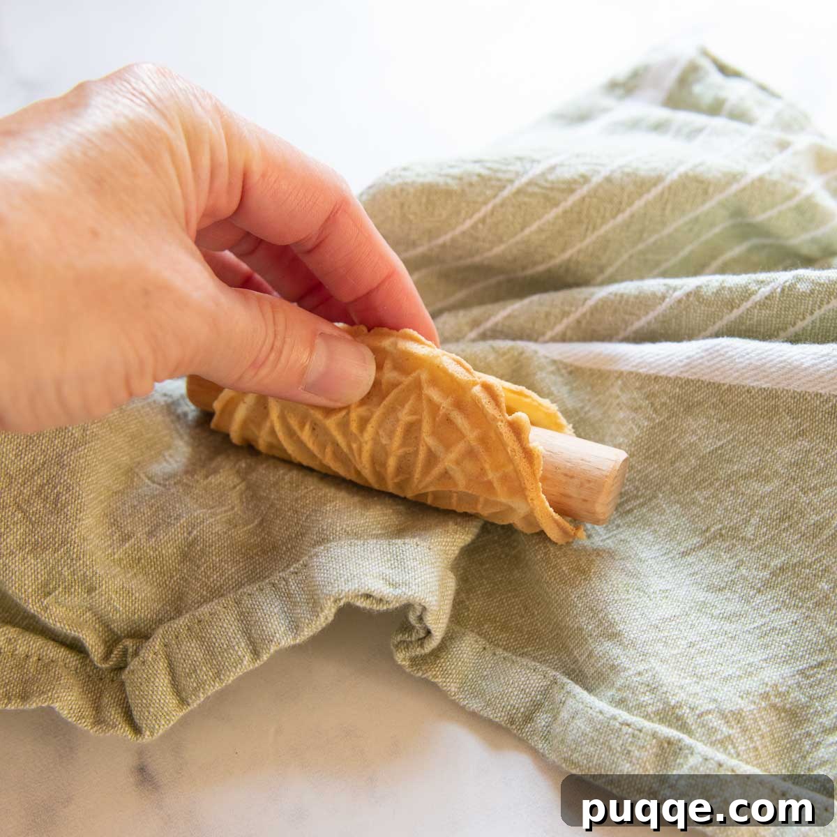 Crispy Gluten-Free Italian Pizzelle Cookies 5 A warm, freshly baked pizzelle being carefully wrapped around a shaping rod to form a cannoli shell.