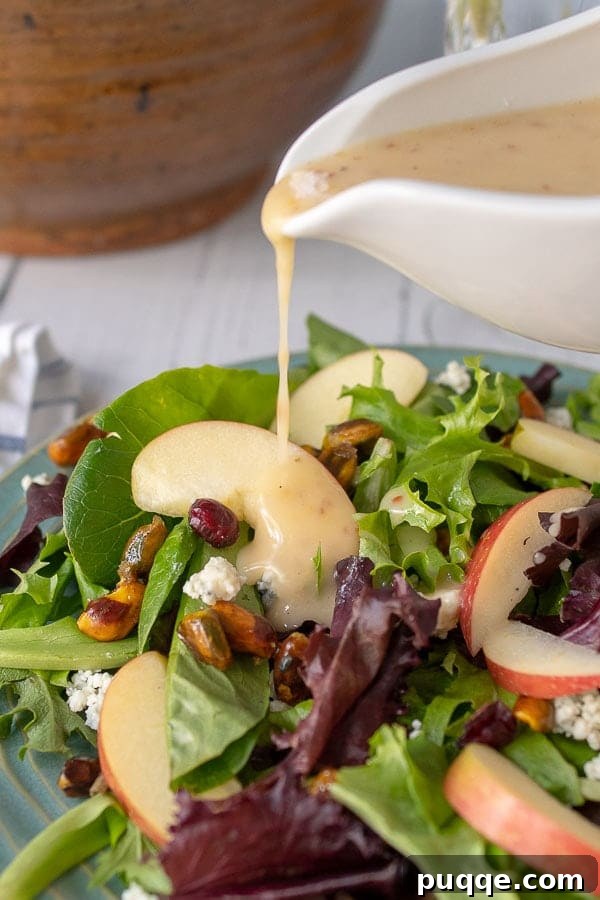 maple vinaigrette being poured from a white dressing container onto the apple pecan salad