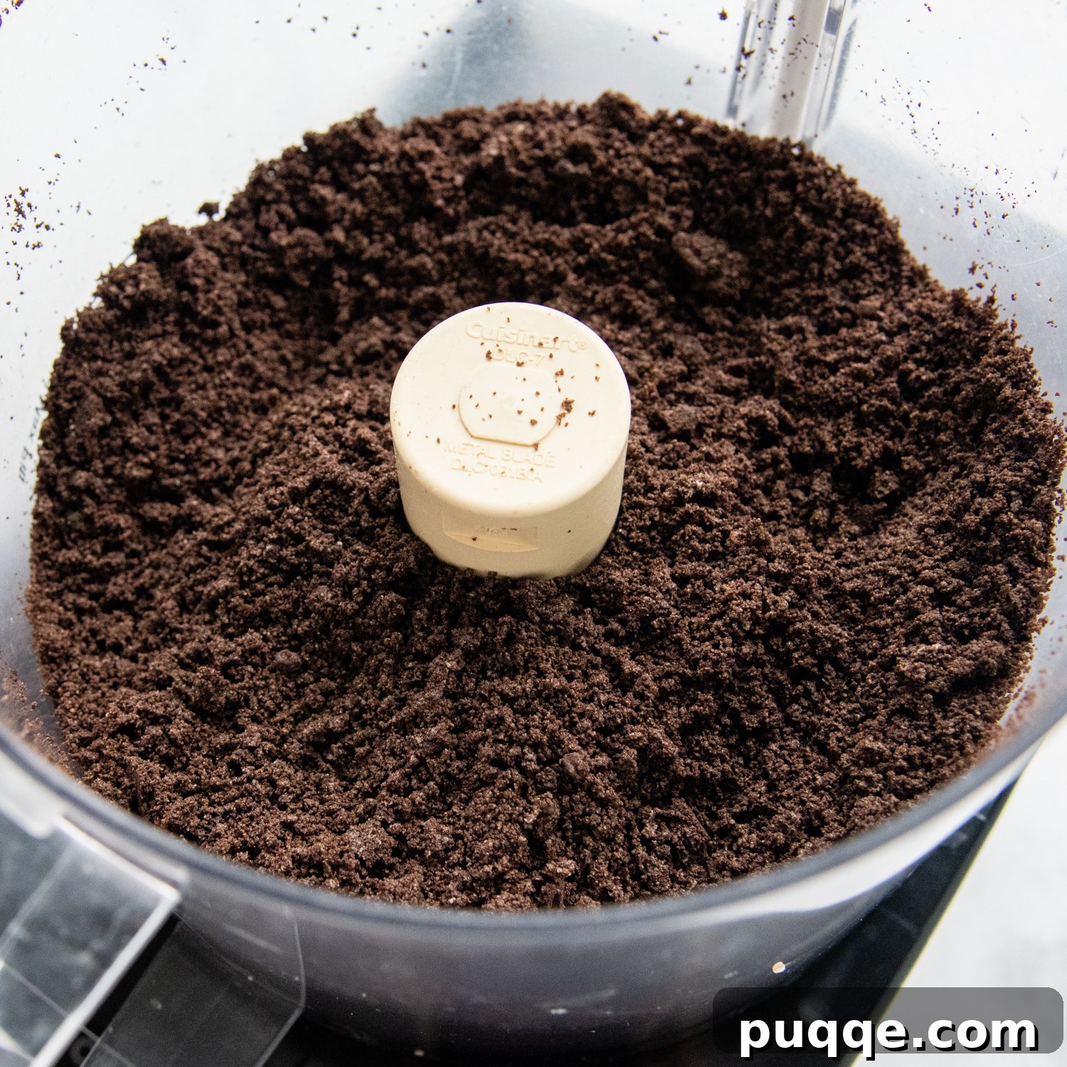 Gluten-free Oreos being crushed into fine crumbs in a food processor, ready for the next step.