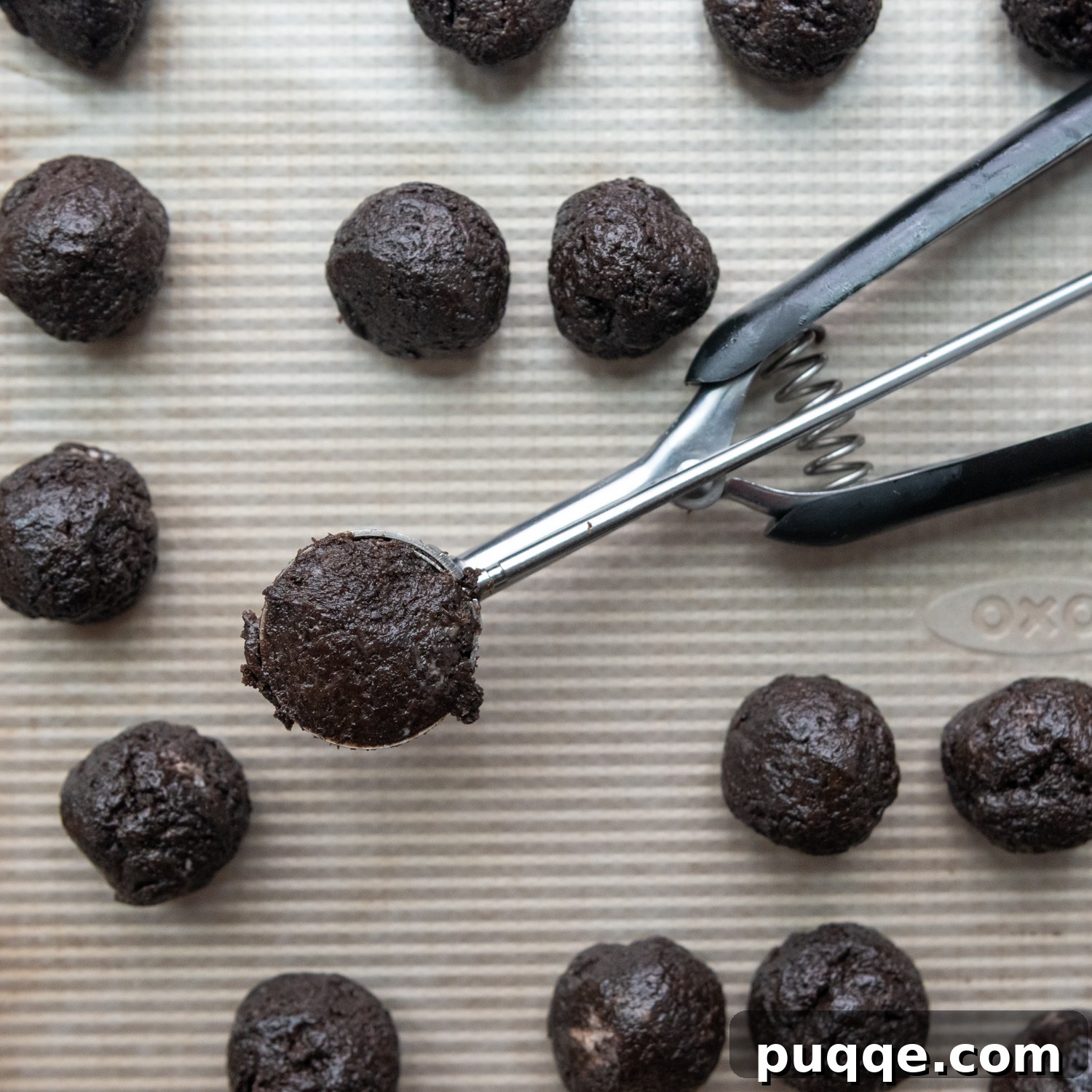 A small cookie scoop precisely dividing the gluten-free Oreo mixture into equal portions on a baking sheet.