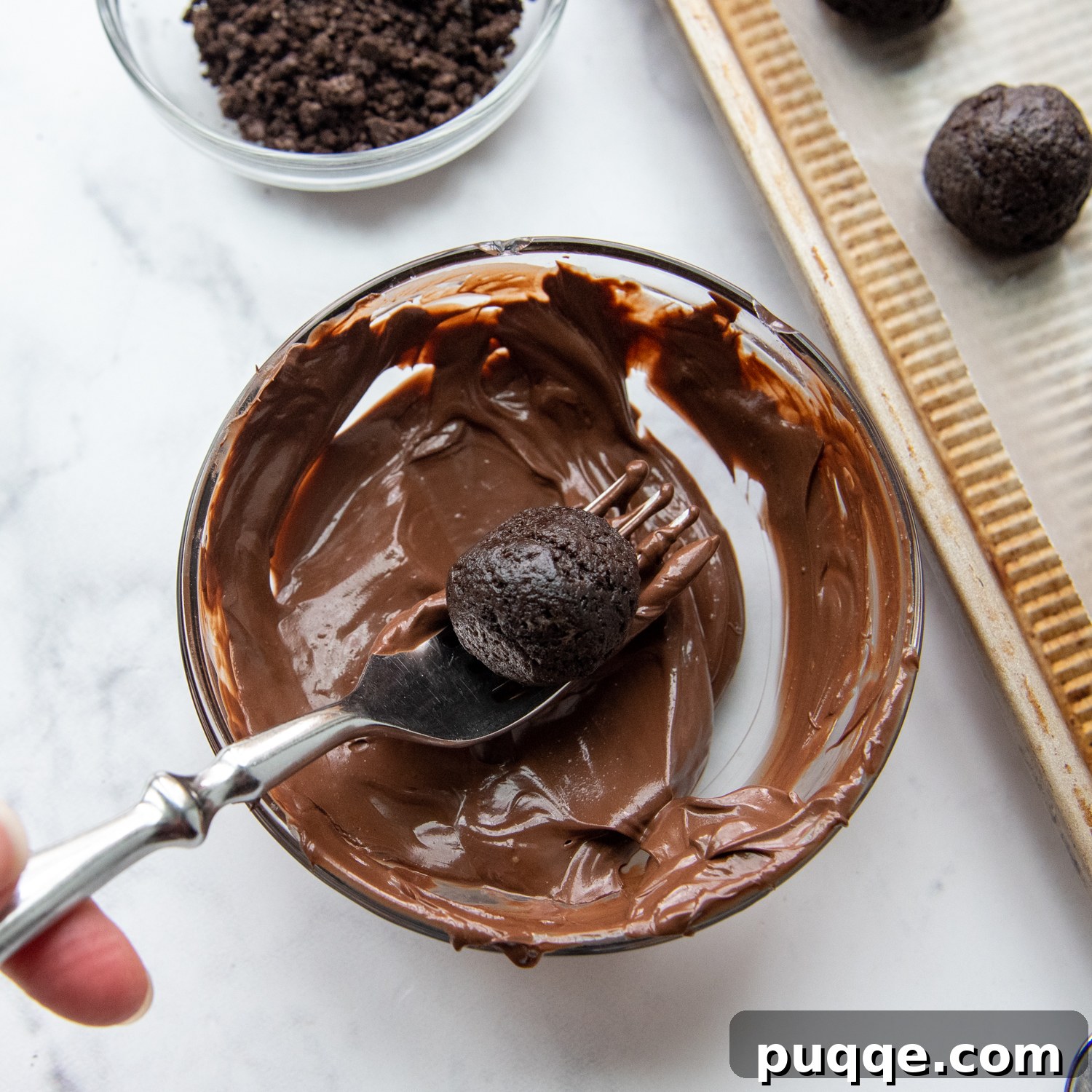 A fork carefully lifting a chocolate-dipped Oreo ball from a bowl of melted chocolate, showing the smooth coating.