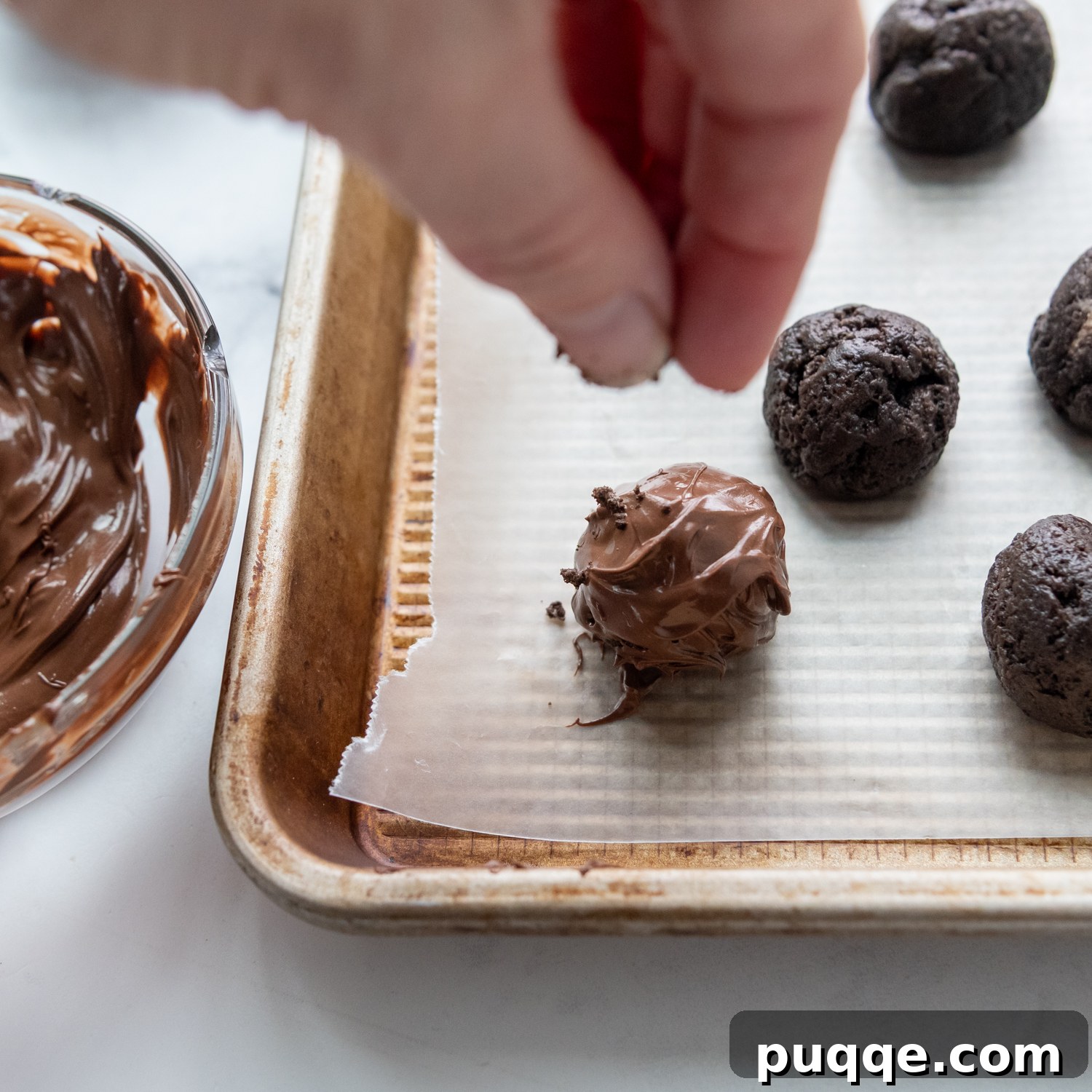 A hand artfully sprinkling crushed Oreo crumbs over a freshly chocolate-dipped truffle on a baking sheet.