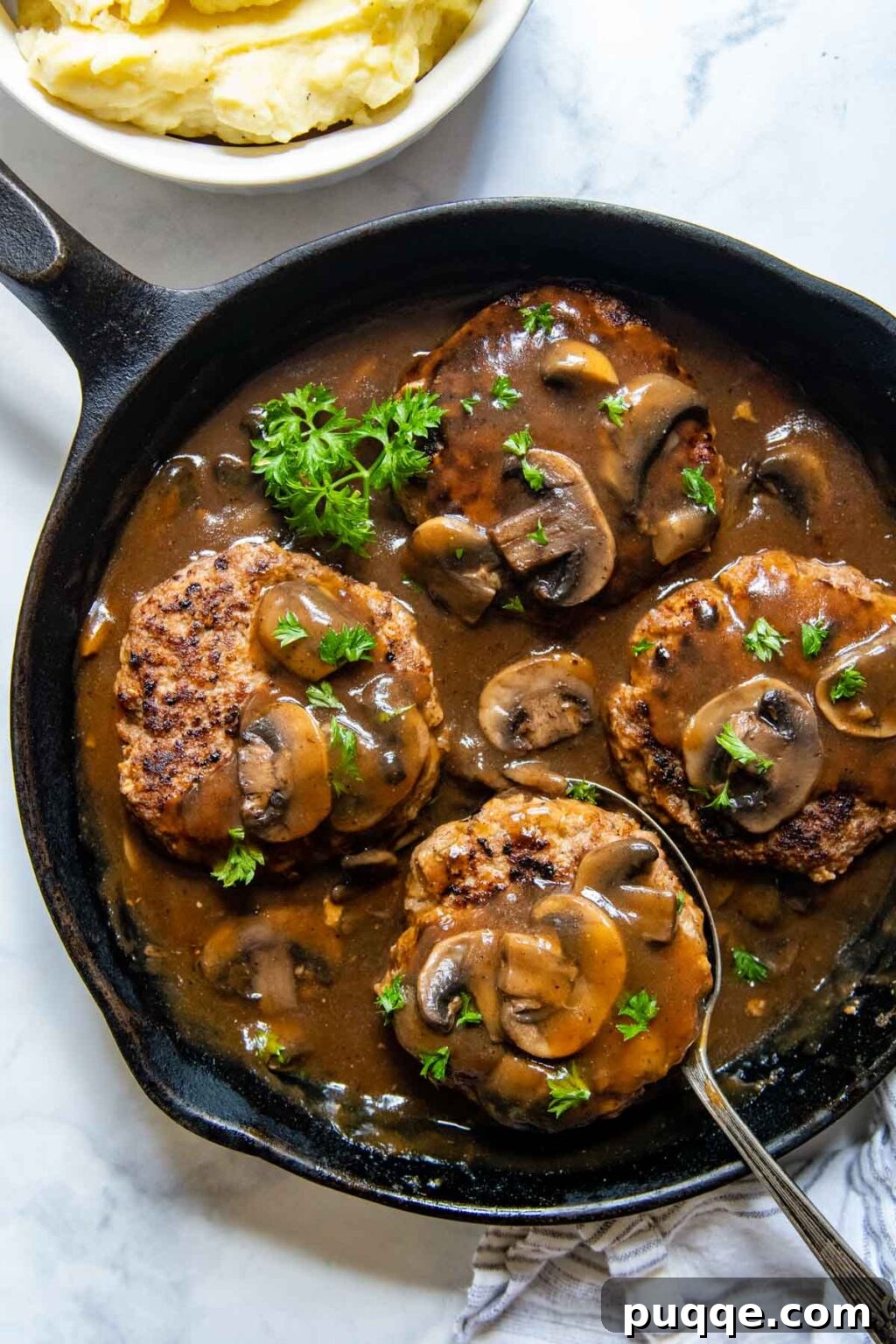 The Ultimate Guide to 50+ Easy Salisbury Steak Sides 3 cooked salisbury steaks with gravy in a cast iron skillet.
