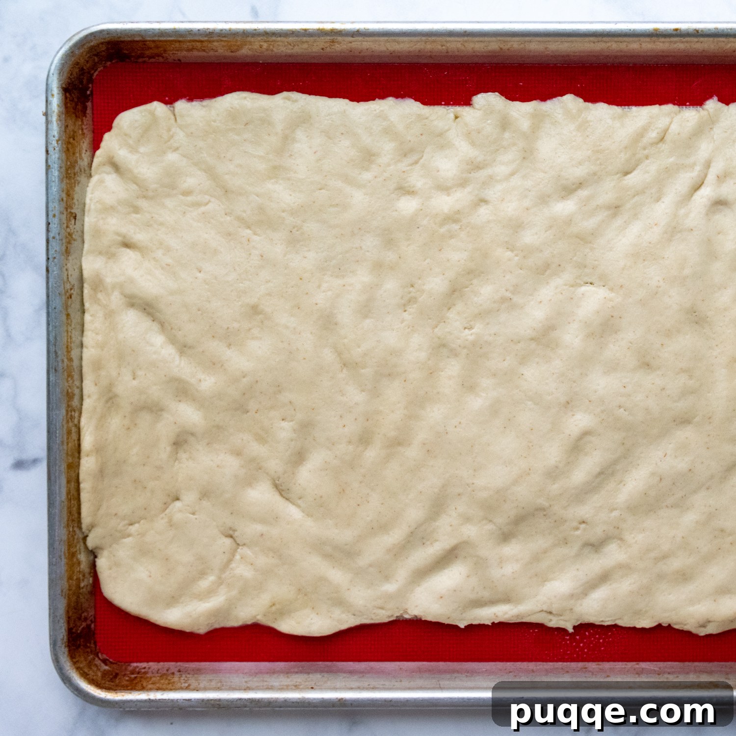 Cloud-Like Gluten-Free Cinnamon Rolls 5 Gluten-free cinnamon roll dough patted into a uniform rectangle on a greased silicone baking mat, ready for filling.