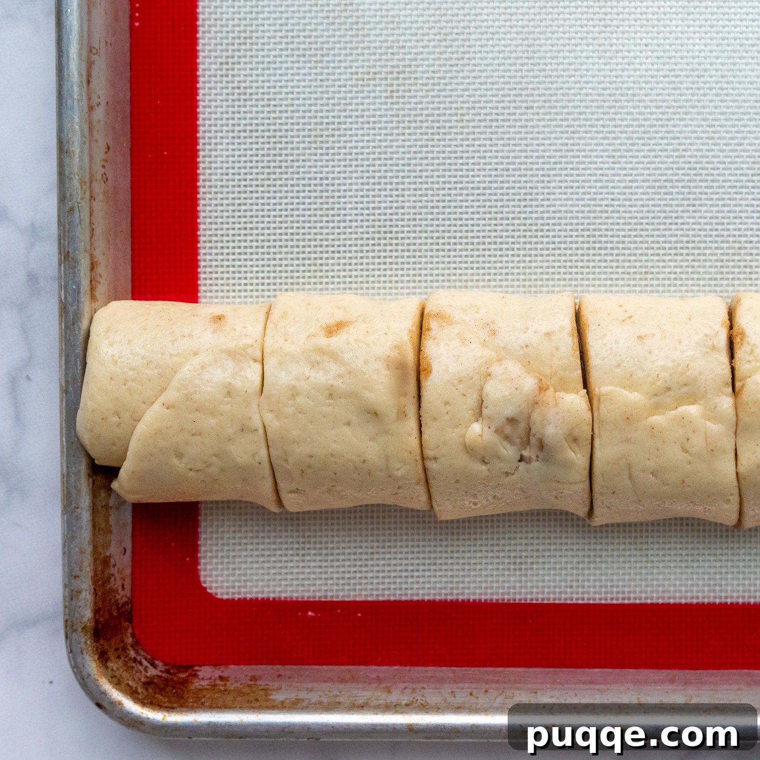 Cloud-Like Gluten-Free Cinnamon Rolls 7 A rolled log of cinnamon roll dough, scored and neatly sliced into nine equal sections, ready for baking.