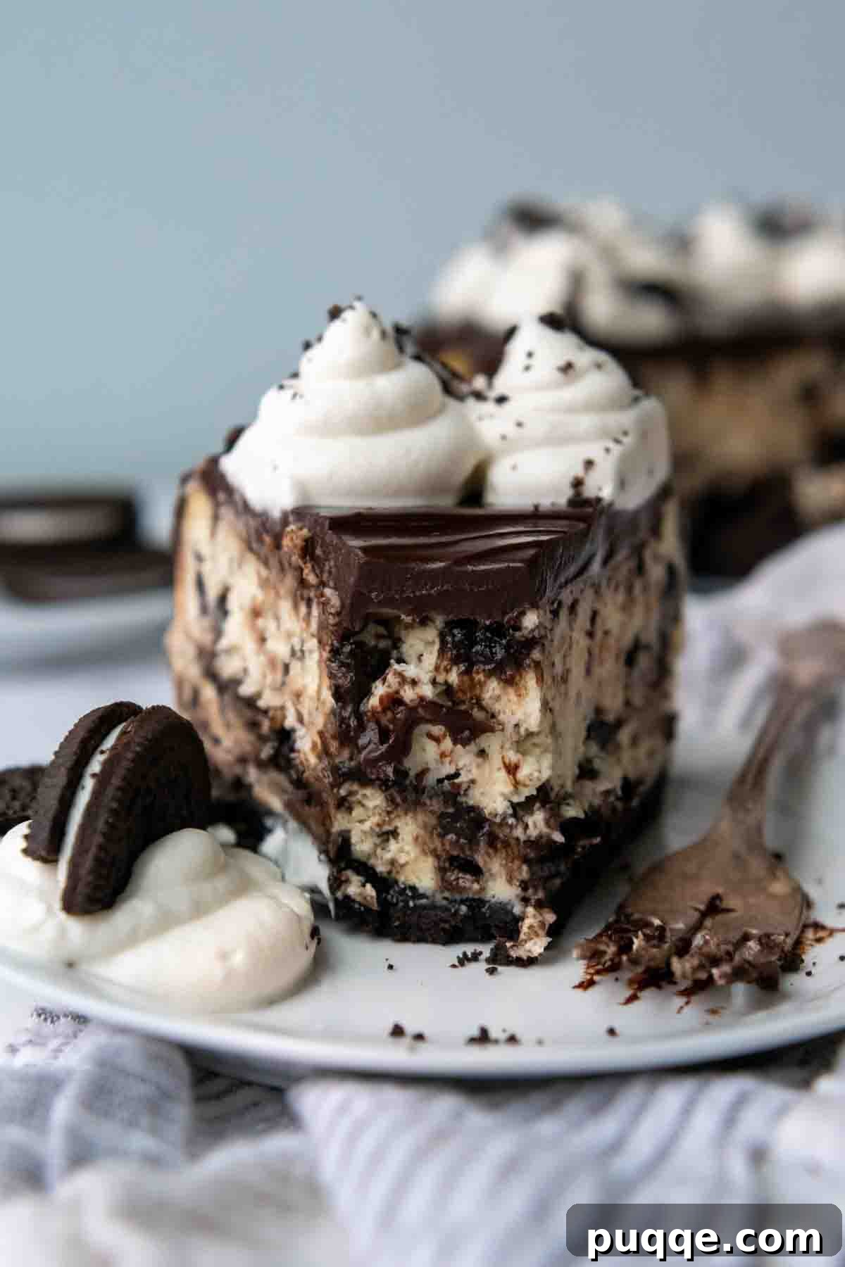 Velvet Smooth Gluten-Free Oreo Cheesecake Bliss 2 A perfectly sliced gluten-free Oreo cheesecake with a bite taken out, served on a white plate, showcasing its creamy filling, chocolate ganache, and whipped cream topping.