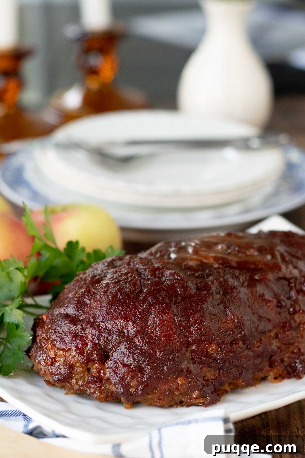 Pork meatloaf on a white serving platter, garnished with fresh herbs and apples in the background.