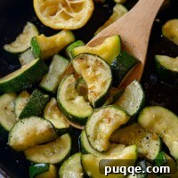 Close up shot of cooked zucchini being held by a wooden spoon, showcasing its perfect texture.