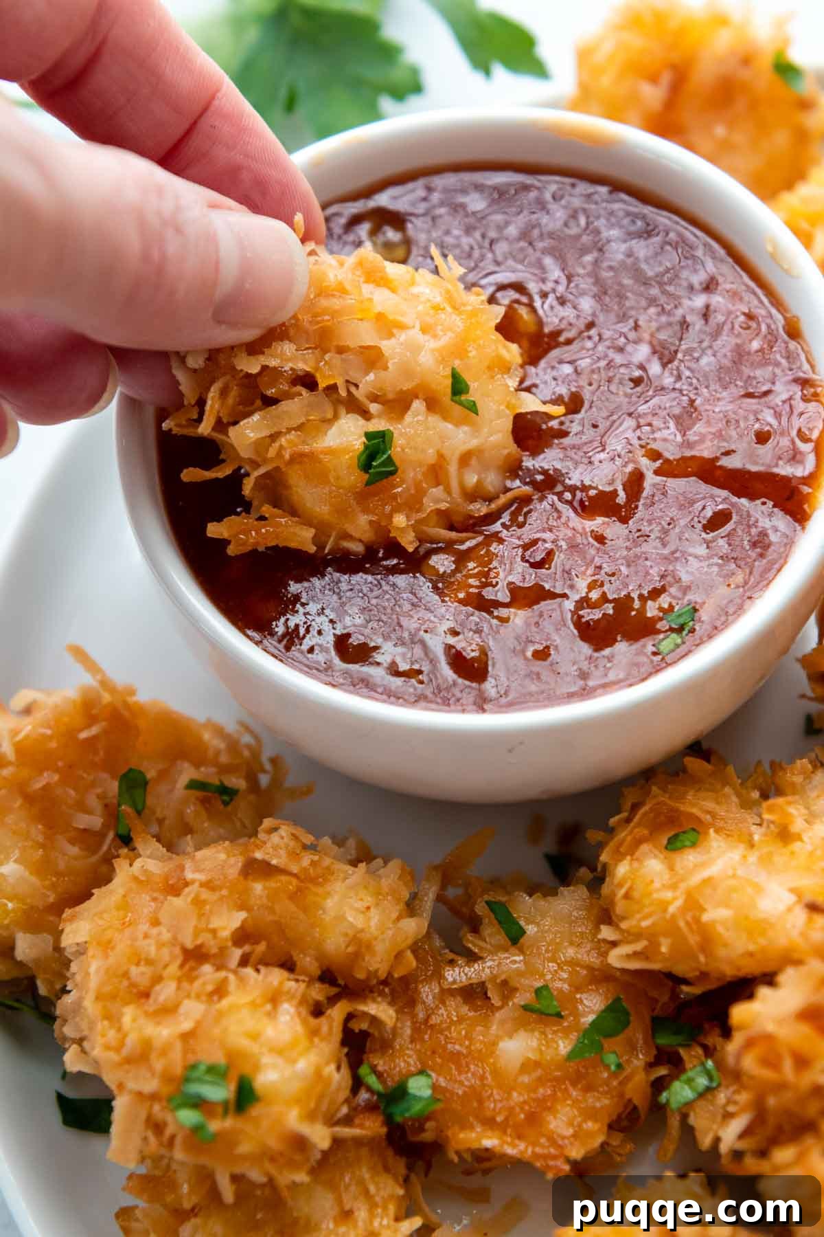 Golden Guilt-Free Coconut Shrimp: Oven or Air Fryer Crisp 6 A crispy coconut shrimp being dipped into a sweet and spicy sauce.
